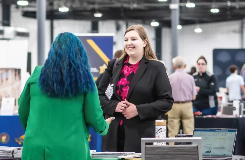 Student speaking with employer at career fair table, smiling.